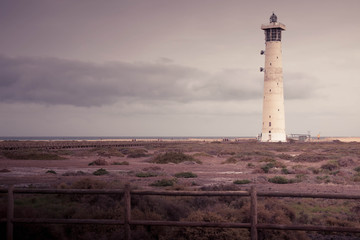 Fototapeta premium Morro Jable lighthouse in Fuerteventura, Canary islands, Spain. Pastel pink lighthouse landscape with copyspace. Vacation, relax or loneliness background or wallpaper.