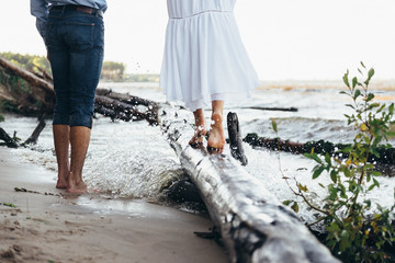 legs of a guy and a girl walking along the beach, the girl is standing on a log under the spray of water