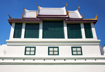 A building in Asian style, part of a house with a roof and windows against a blue sky. Bangkok, Thailand.