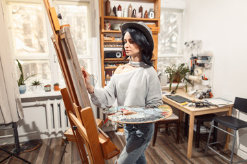 Smiling girl paints on canvas with oil colors in workshop
