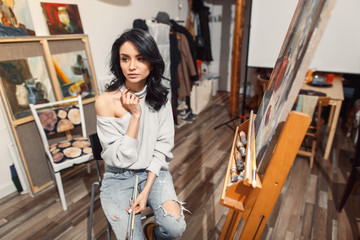 Smiling girl paints on canvas with oil colors in workshop