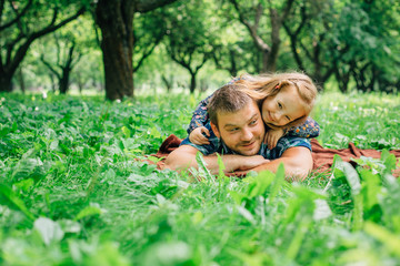 Little girl lying on her father in the park. Green grass. Happy parenting concept.