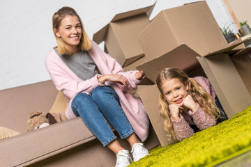 happy mother and daughter having fun with cardboard boxes while relocating