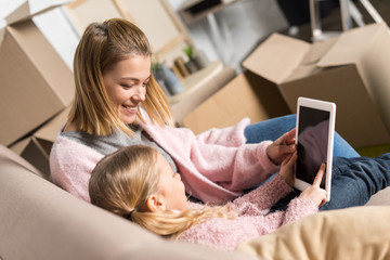 happy mother and daughter using digital tablet with blank screen while moving home