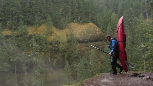 Handheld shot of whitewater kayaker with kayak walking on mountain in forest