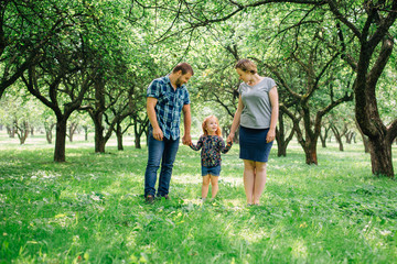 Fototapeta premium Cute young happy family having fun in the park. Little girl with parents outdoors. Mother father and daughter.