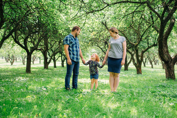 Fototapeta premium Cute young happy family having fun in the park. Little girl with parents outdoors. Mother father and daughter.