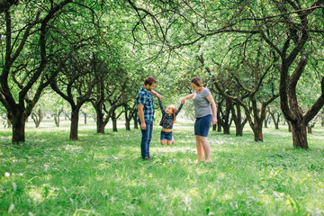 Fototapeta premium Cute young happy family having fun in the park. Little girl with parents outdoors. Mother father and daughter.