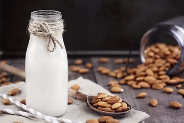 Fotobehang Organic white almond milk in a glass bottle with whole almonds spilled over a rustic wooden table. © Stephanie Frey