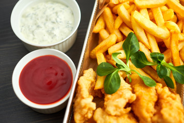chicken nuggets with french fries and different sauces on wooden board,