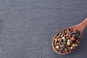 Chinese pepper, Sichuan pepper in wooden spoon on black slate stone plate