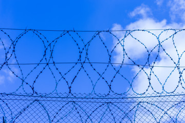 Gray fence with barbed wire in the background of a blue sky with clouds