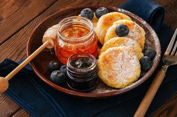 Top view of homemade cottage cheese pancakes- syrniki in a plate, jam on a wooden backdrop.