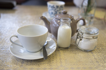 Fototapeta na wymiar Cup and saucer with a teapot, milk and sugar, in a café setting