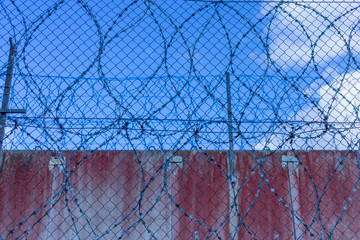 Roll of razor wire on concrete wall. Barbed wire on the wall. Prison wall against blue sky