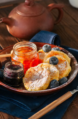 Top view of homemade cottage cheese pancakes- syrniki in a plate, jam on a wooden backdrop.