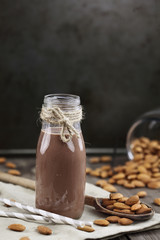 Organic chocolate almond milk in a glass bottle with whole almonds spilled over a rustic wooden table.