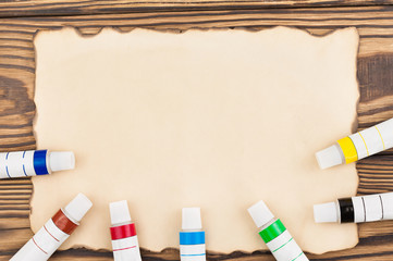 Lot of colorful acrylic paints in closed tubes on burnt rectangle blank paper on old wooden brown boards. Top view