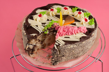 Dissected tasty round chocolate cake on shiny metal grid on pink background