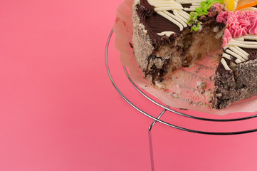 Dissected tasty round chocolate cake on shiny metal grid on pink background