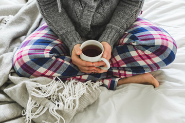 Woman in cozy pyjamas sat on bed with warm cup of tea