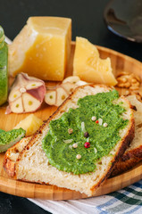 Bruschetta with basil walnut pesto sauce on a wooden plate. Black stone backdrop.