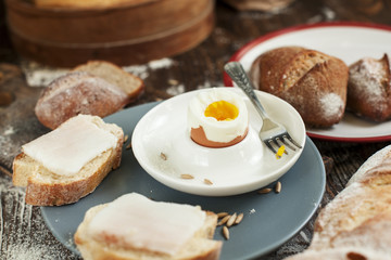 boiled egg on a plate, freshly baked bread and sandwiches with bacon on a wooden table