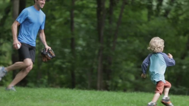 Cheerful father chasing and lifting son while playing baseball at yard
