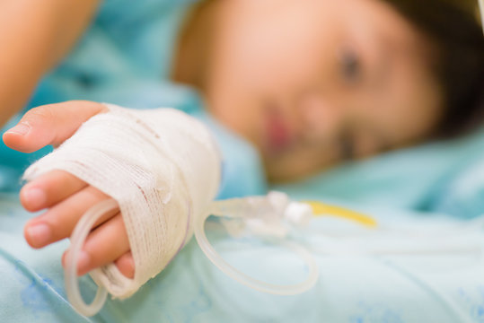 Closeup kid hand  sleeps on a bed in hospital with saline intravenous, selective focus.