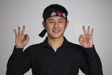 Retrato de un Asiatico con una bandana negra haciendo signo positivo.