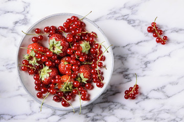 Fresh berries mix (strawberry and red currant) in ceramic bowl on grey marble table. Selective focus 