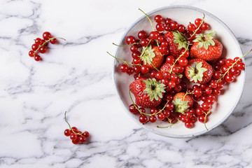 Fresh berries mix (strawberry and red currant) in ceramic bowl on grey marble table. Selective focus 