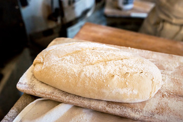 Fresh uncooked organic bread with white flour on it on a wooden peel