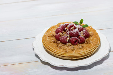 traditional thin pancakes with fresh raspberries on plate on wooden table