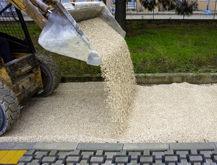 skid loader distributes grit and sand for the background of the pavement paving