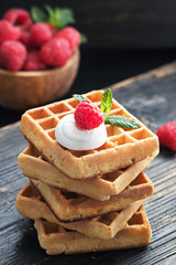 Waffles with summer raspberries served on black old rustic background.