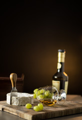 Still life of grapes, Cognac and french cheese on a wooden board