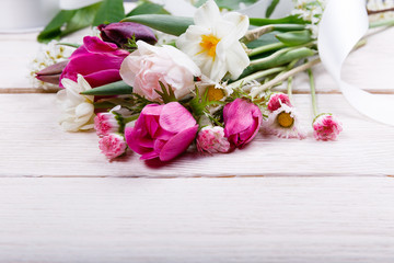 Bouquet first spring flowers, pink, purple tulips, daffodils and daisies on white wooden background.