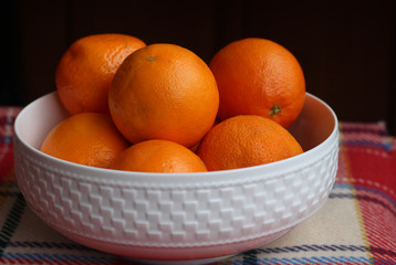 White china bowl filled with succulent juicy fresh oranges on an a checkered red blanket.Black background.
