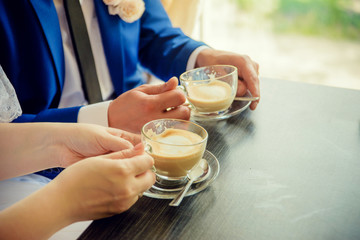 two cups of cappuccino in the hands of a boy and a girl at a table in a cafe