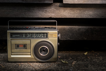 Vintage stereo in the 90s put on cement floor at roadside with wood background. The light goes down on the stereo.
