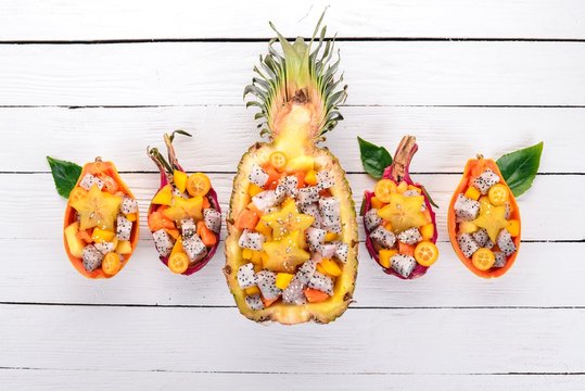 Exotic fruit salad served in half a pineapple. Papaya, Dragon Fruit, tamarind, cactus fruit, mango, mangosteen On a wooden background. Top view.
