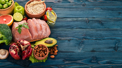 Healthy food. Raw meat, avocado, broccoli, fresh vegetables, nuts and fruits. On a wooden background. Top view. Copy space.