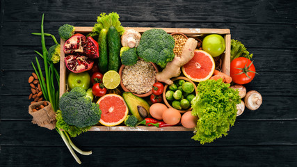 The concept of healthy food. Fresh vegetables, nuts and fruits in a wooden box. On a wooden background. Top view. Copy space.