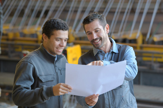 male supervisor with worker discussing over blueprints in industry