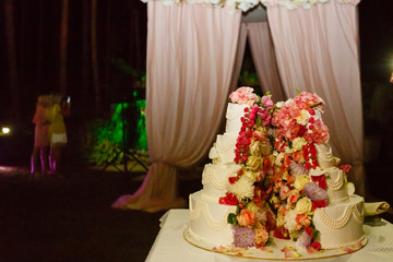 Original wedding cake in the middle of flowers stands on the white table in the middle of restaurant hall