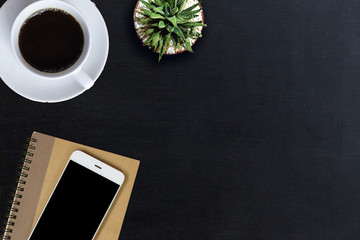 Office desk with notepad,smartphone, coffee and plant. Top view of black office desk. Business desk of Designer or Journalist modern and minimal lifestyle concept.