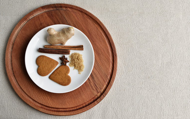 sweet valentines. valentines day A star anise, ginger cookies in the shape of heart, two cinnamon sticks, brown sugar, a ginger root lie on a white plate on a round wooden background. place for text