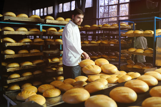 young handsome guy baker pulls out of the oven fresh bread at the bakery background