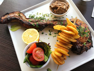 Grilled pork rib, vegetables and fried potatoes on white plate.